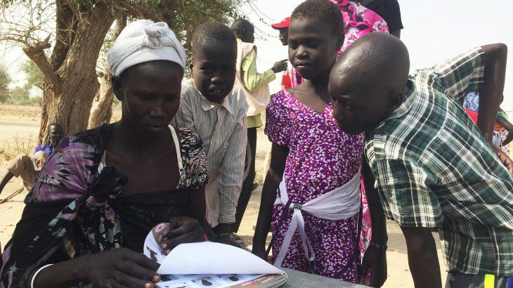 A group of people in Leer review a book containing photos of South Sudanese children located in the neighbouring countries
