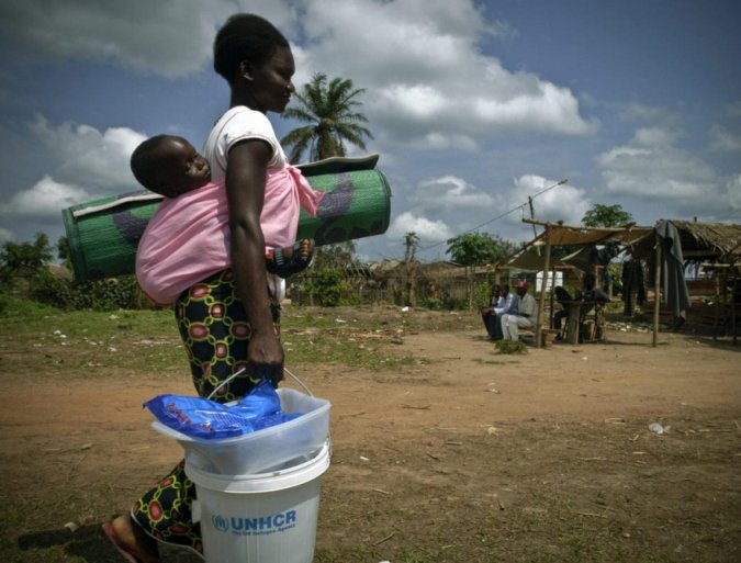 A refugee mother carries her child and relief items in Congo-Brazzaville.