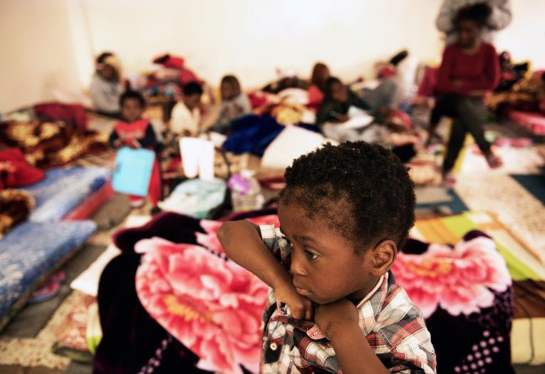 A child stands in a room where women and children sleep on old mattresses laid on the floor at a detention centre in Libya